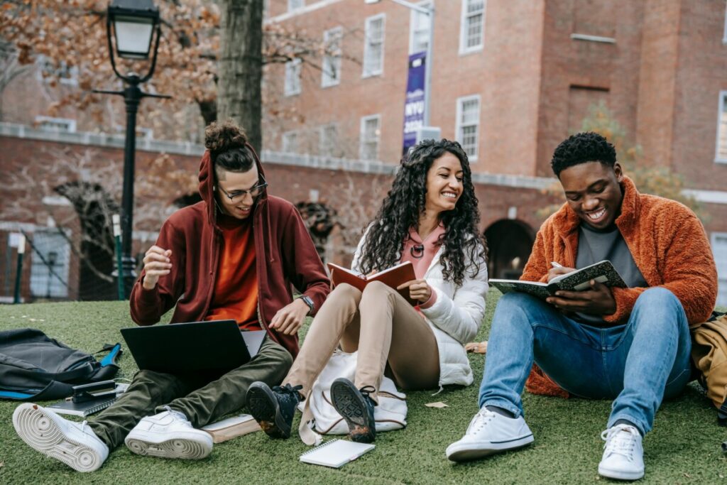 Studying in Australia,Full body of happy diverse students with notebooks and laptop sitting on grassy lawn on campus of university while studying together